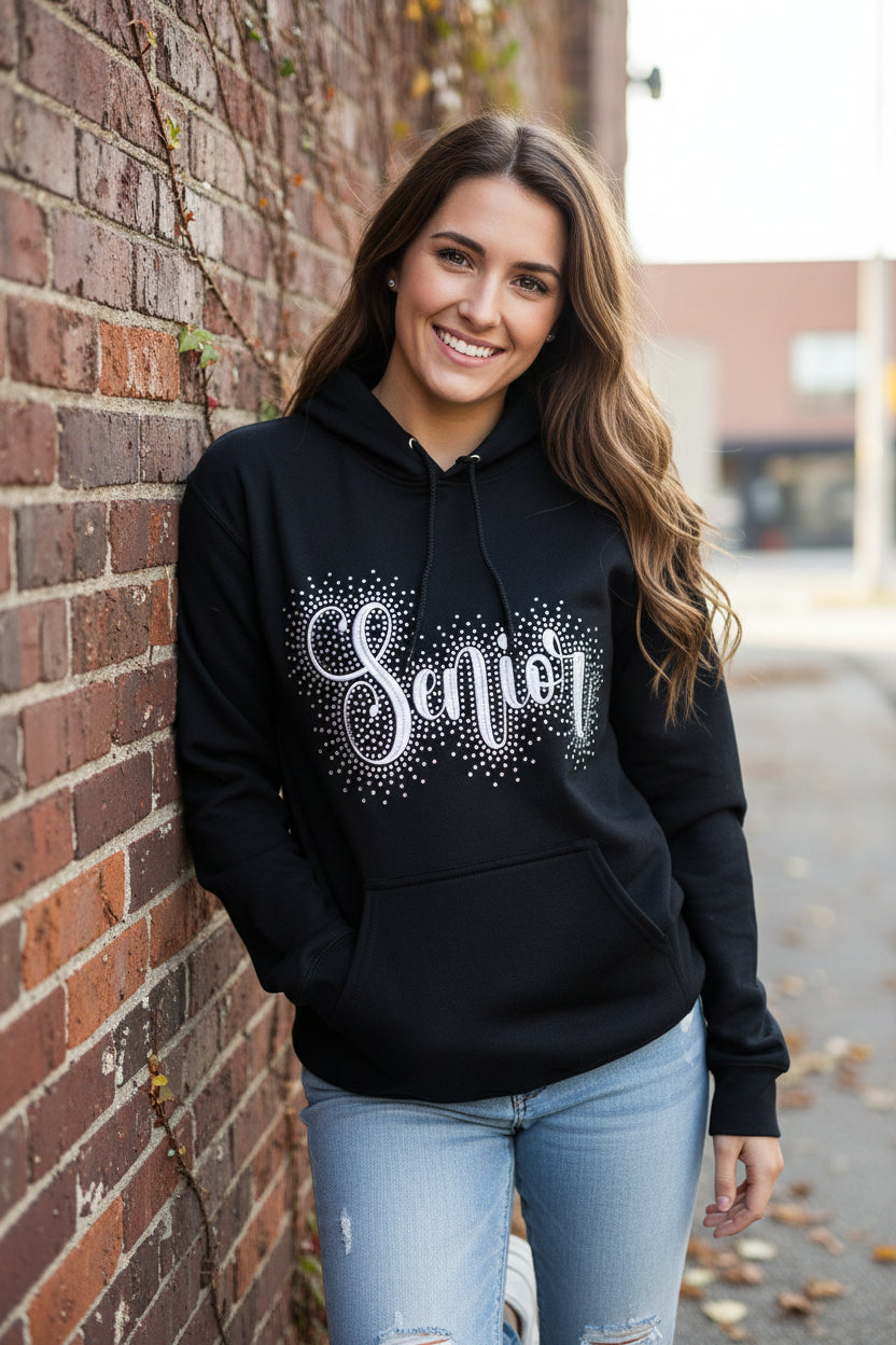 A Black hoodie with Senior embroidered a cross it accented with rhinestones around the word.  