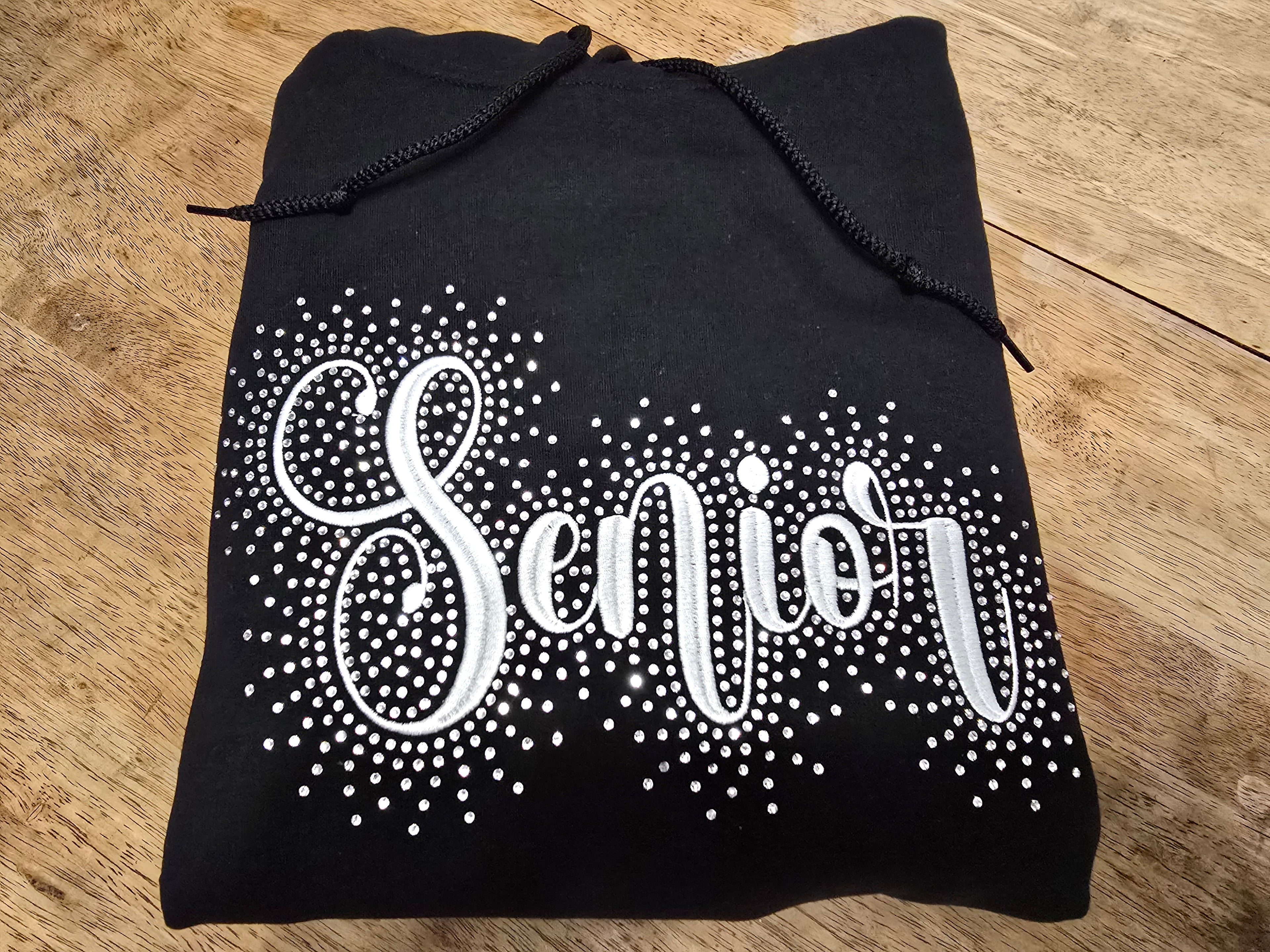 A Black hoodie with Senior embroidered a cross it accented with rhinestones around the word.  